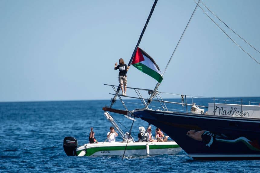Multiple activists and international delegates waving from the deck of a maritime vessel as it departs on a mission to challenge the blockade.